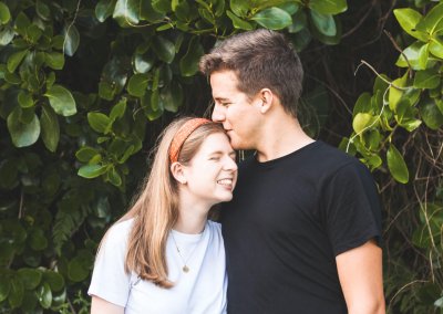 A young man kissing his girlfriend's forehead in front of a tree