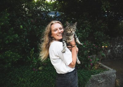 A young woman holding a cat with a backdrop of foliage