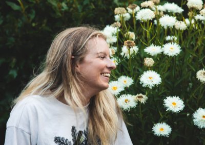 Profile shot of a young woman smiling with a flower bush in the background
