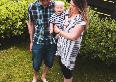 A mother and father stand in the garden smiling at their young son