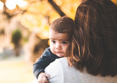 A young baby looks behind his mother's shoulder