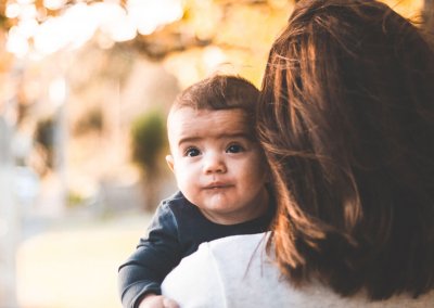 A young baby looks behind his mother's shoulder