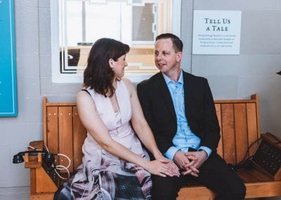 A couple sit together on a bench, smiling at each other